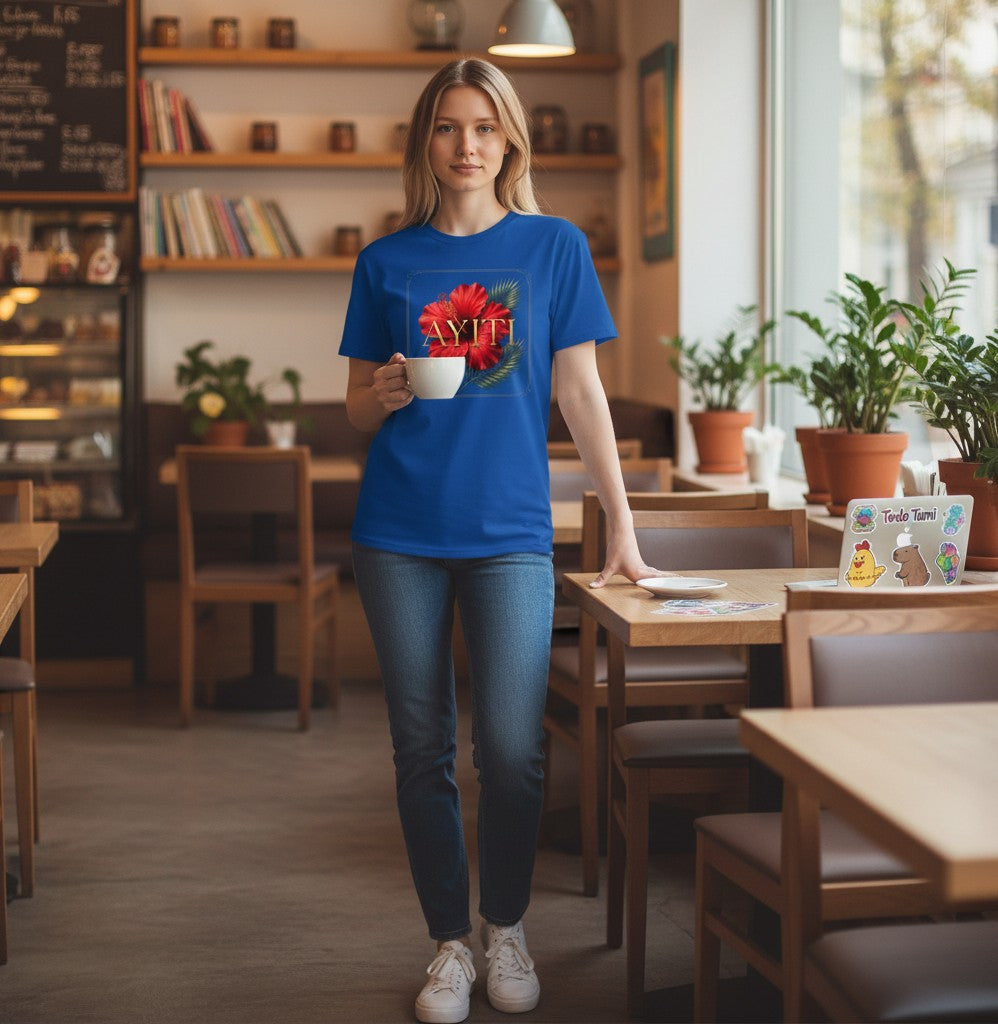 Woman wearing a blue Todo Tumi crewneck t-shirt with a red hibiscus and gold AYITI graphic in a cozy cafe setting.