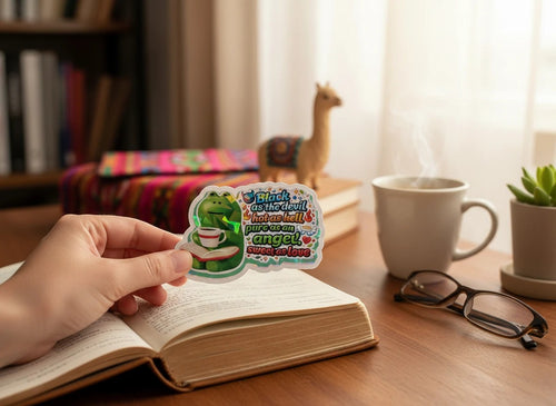 Todo Tumi holographic coffee frog sticker with text Black as the devil, hot as hell on a book held by a hand.