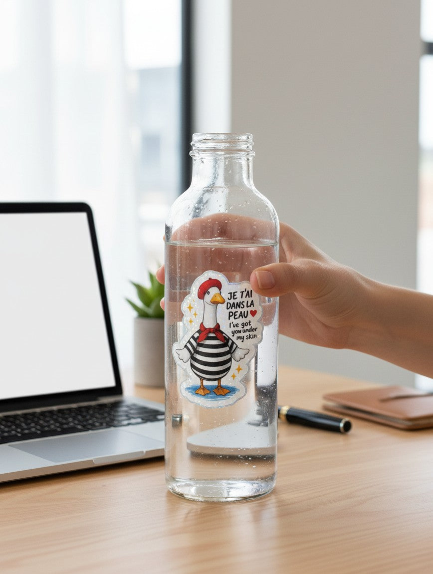 Todo Tumi holographic goose sticker with a French beret and striped shirt on a clear water bottle at a desk.