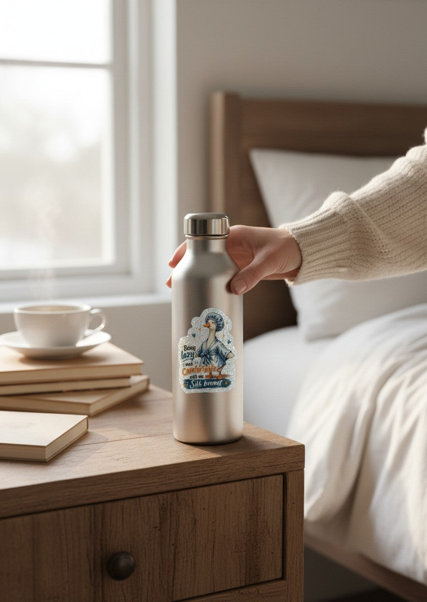 Todo Tumi holographic vinyl sticker of a duck in a blue robe and bonnet on a silver water bottle in a cozy bedroom.